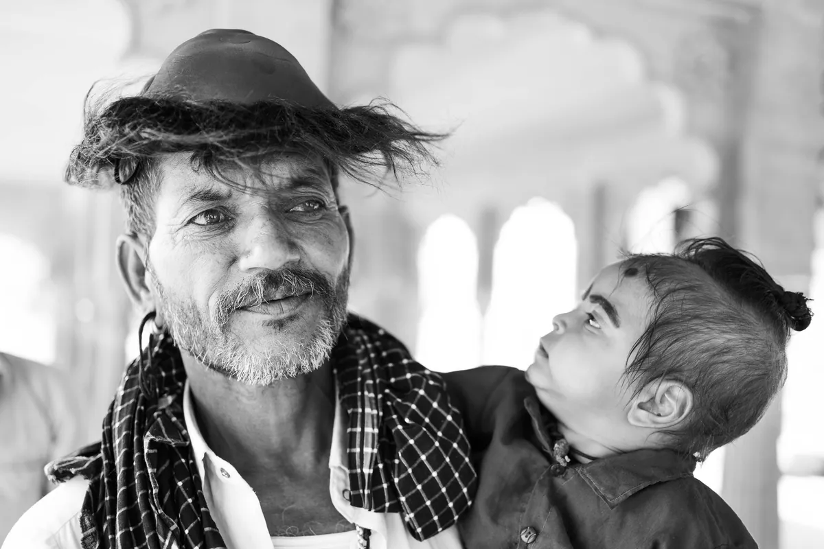 Unknown Man. Performing a religious bathing ceremony with his family in Pushkar. He saw my camera and asked me to take a photo of him, holding his child. The time it took me to bring the camera up to my eye, he had quickly grabbed a plastic monkey mask his friend was holding and placed it on his head like a hat, with his son looking as confused as I was. Pushkar Lake, Pushkar, India
